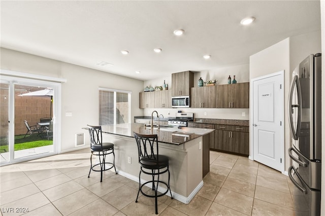 kitchen with sink, an island with sink, a kitchen bar, light tile patterned floors, and appliances with stainless steel finishes