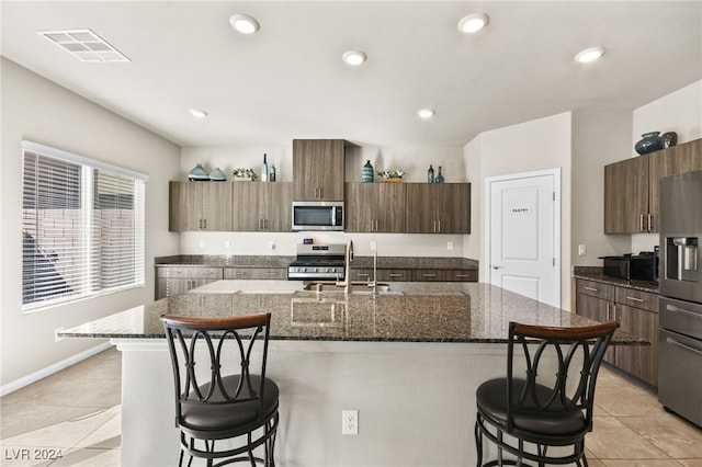 kitchen featuring a kitchen bar, appliances with stainless steel finishes, dark stone counters, sink, and an island with sink