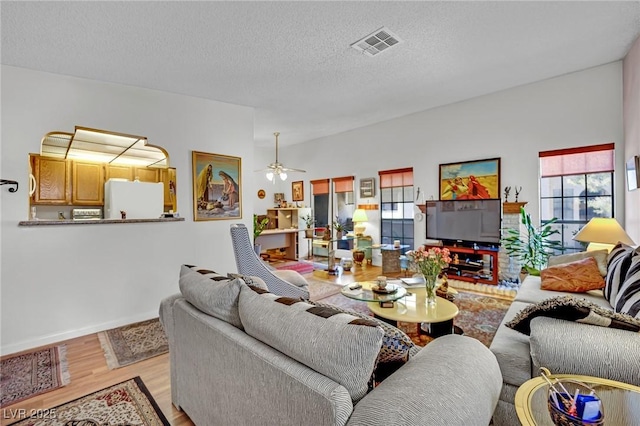 living room with ceiling fan, light hardwood / wood-style floors, and a textured ceiling