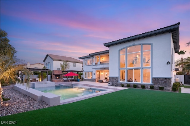 back house at dusk featuring a lawn, a gazebo, a swimming pool with hot tub, a balcony, and a patio