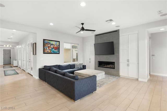 living room with a fireplace, light wood-type flooring, and ceiling fan