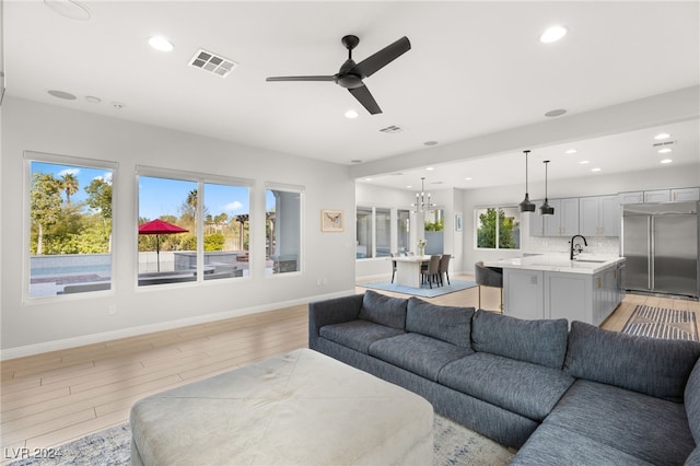 living room with ceiling fan with notable chandelier, light hardwood / wood-style floors, and sink