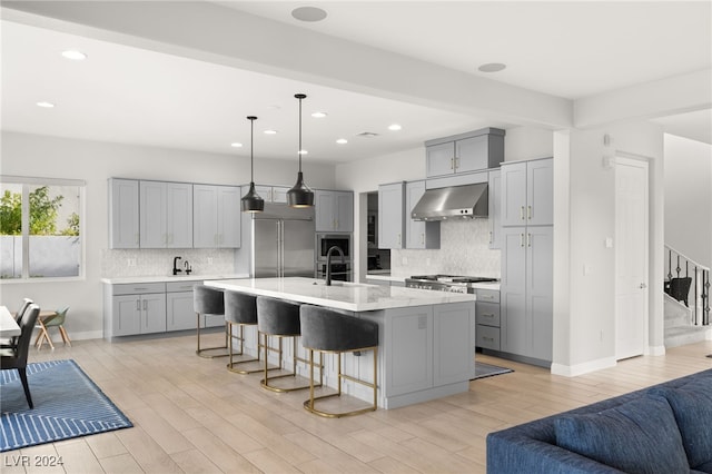 kitchen featuring pendant lighting, wall chimney exhaust hood, gray cabinets, an island with sink, and high quality fridge