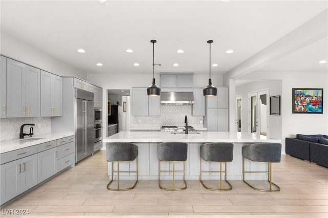 kitchen featuring gray cabinetry, an island with sink, and wall chimney range hood