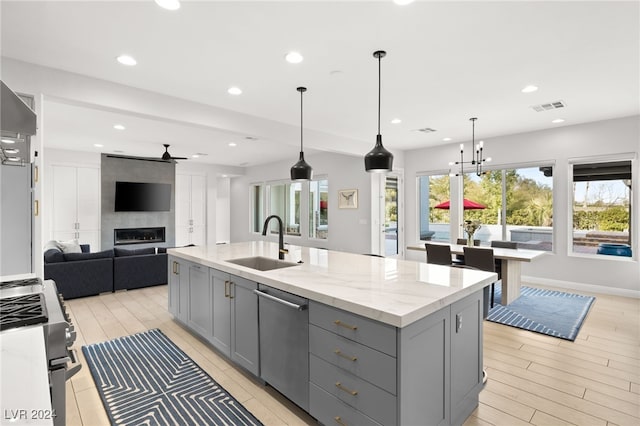 kitchen featuring light stone counters, stainless steel appliances, sink, a center island with sink, and hanging light fixtures