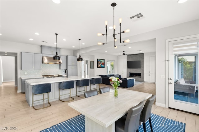 dining room with a tiled fireplace, sink, a chandelier, and light hardwood / wood-style flooring