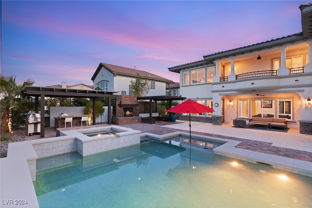 back house at dusk with an outdoor living space with a fireplace, a swimming pool with hot tub, a balcony, area for grilling, and a patio