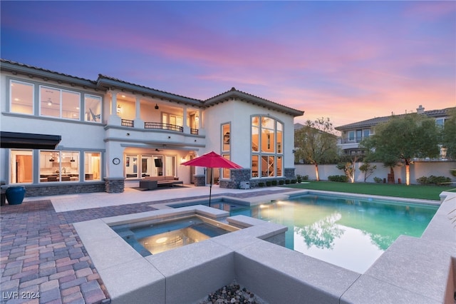 back house at dusk with outdoor lounge area, a swimming pool with hot tub, a balcony, and a patio area