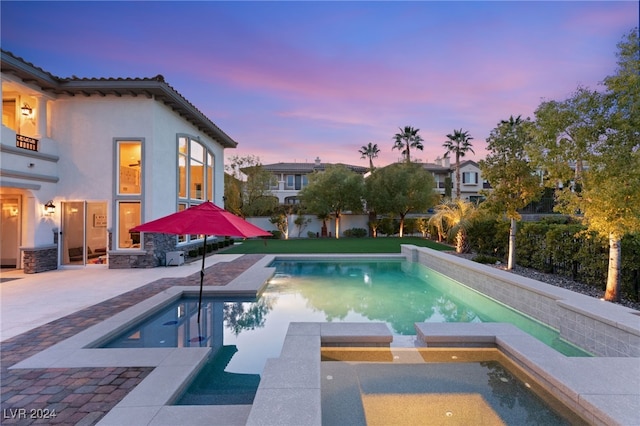 pool at dusk featuring a patio area and an in ground hot tub