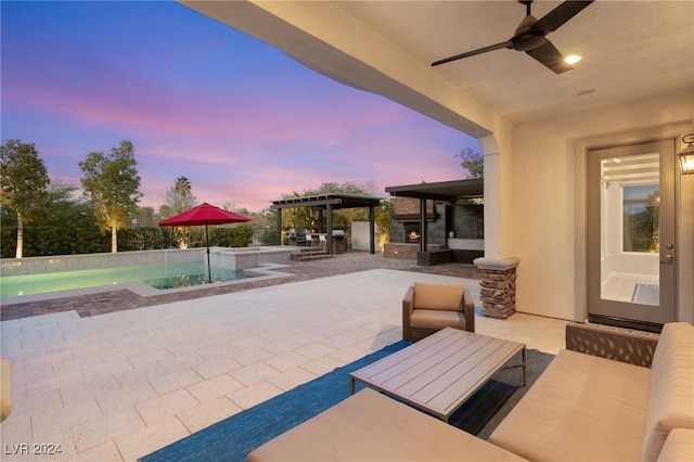 patio terrace at dusk with an outdoor living space with a fireplace, an outdoor kitchen, and ceiling fan