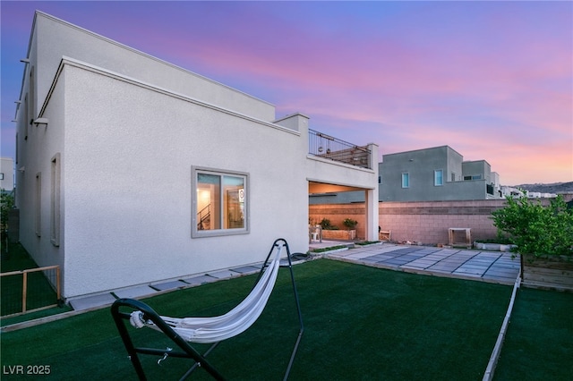 back house at dusk with a lawn and a patio