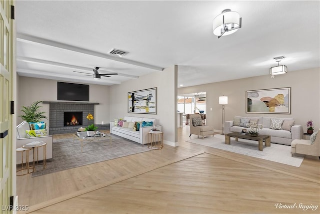 living room featuring beam ceiling, ceiling fan, light hardwood / wood-style flooring, and a brick fireplace