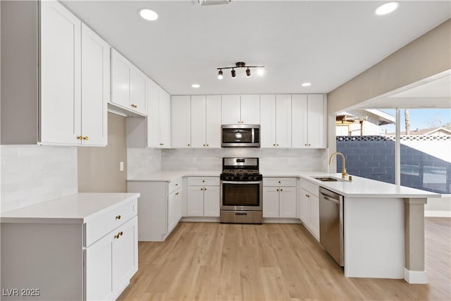 kitchen with white cabinets, sink, decorative backsplash, light hardwood / wood-style floors, and stainless steel appliances