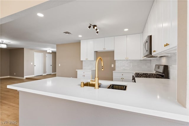 kitchen featuring kitchen peninsula, stove, backsplash, sink, and white cabinets