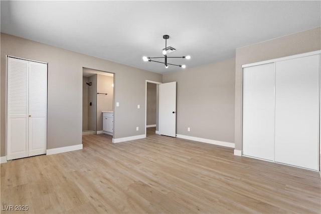 unfurnished bedroom featuring ensuite bath, a chandelier, two closets, and light hardwood / wood-style floors