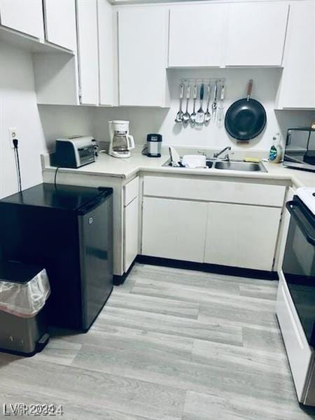 kitchen with stove, refrigerator, sink, white cabinets, and light hardwood / wood-style floors