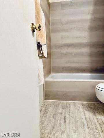 bathroom with a washtub, hardwood / wood-style floors, and toilet