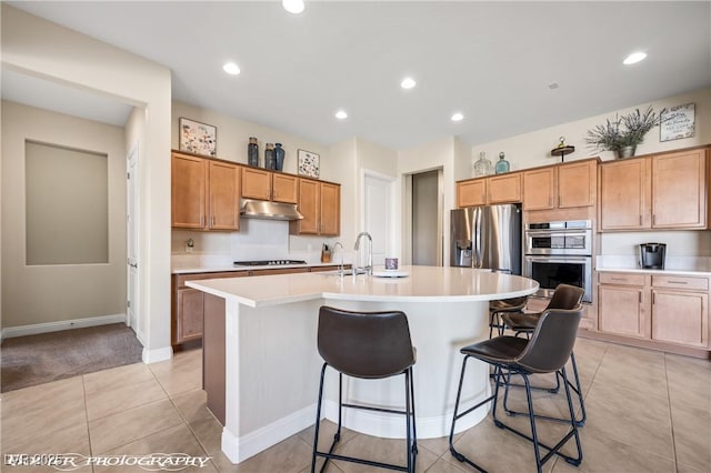 kitchen featuring appliances with stainless steel finishes, a breakfast bar, sink, light tile patterned floors, and an island with sink