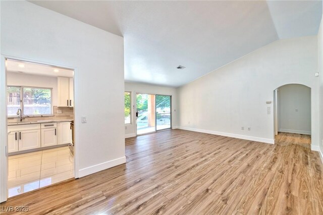 unfurnished living room with vaulted ceiling, light hardwood / wood-style flooring, and sink