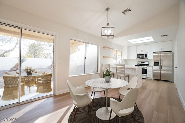 dining area with light hardwood / wood-style floors, lofted ceiling, and an inviting chandelier