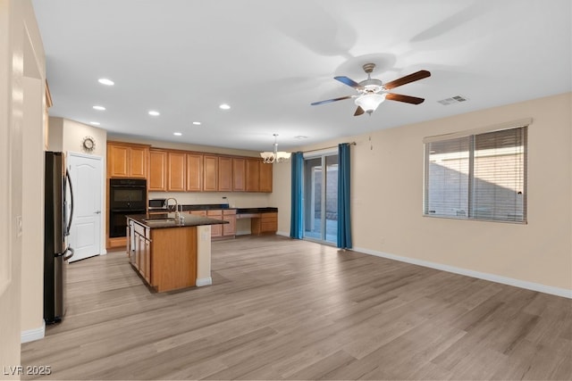 kitchen featuring a center island with sink, pendant lighting, light wood-type flooring, and double oven