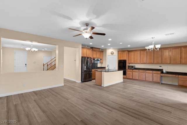 kitchen with light wood-type flooring, stainless steel appliances, sink, pendant lighting, and a center island with sink