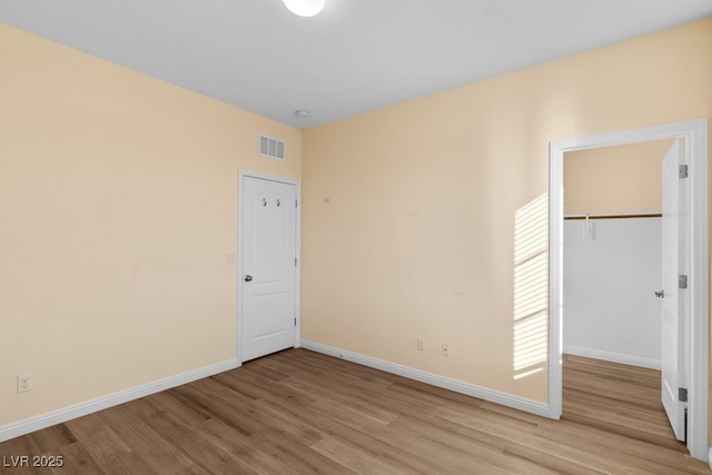 unfurnished bedroom featuring a closet, light hardwood / wood-style flooring, and a spacious closet