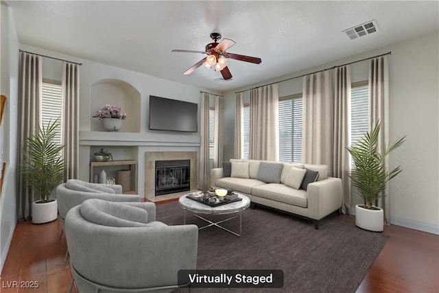 living room with a tile fireplace, dark hardwood / wood-style floors, built in features, and ceiling fan