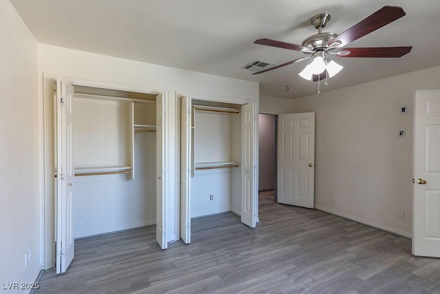 unfurnished bedroom with multiple closets, ceiling fan, and hardwood / wood-style floors