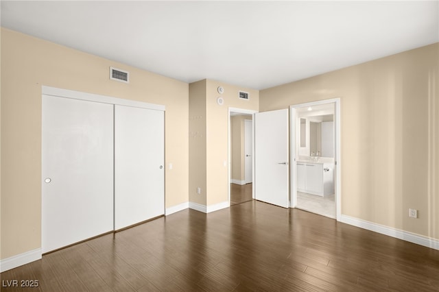 unfurnished bedroom with a closet, dark hardwood / wood-style floors, and connected bathroom