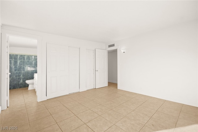 unfurnished bedroom with ensuite bath, tile walls, and light tile patterned flooring