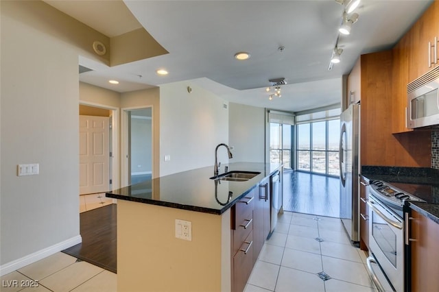 kitchen featuring appliances with stainless steel finishes, dark stone counters, a kitchen island with sink, sink, and light tile patterned flooring