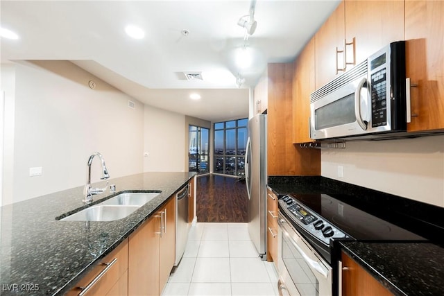 kitchen with dark stone counters, rail lighting, sink, light tile patterned floors, and stainless steel appliances