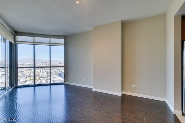 unfurnished room featuring a mountain view, dark hardwood / wood-style flooring, and a wall of windows