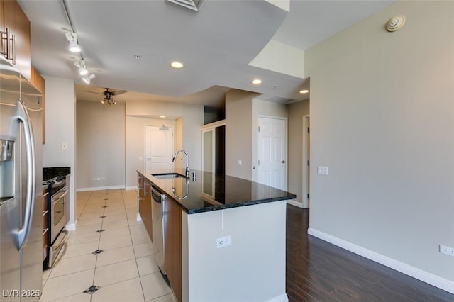 kitchen with appliances with stainless steel finishes, a kitchen island with sink, dark stone counters, and sink