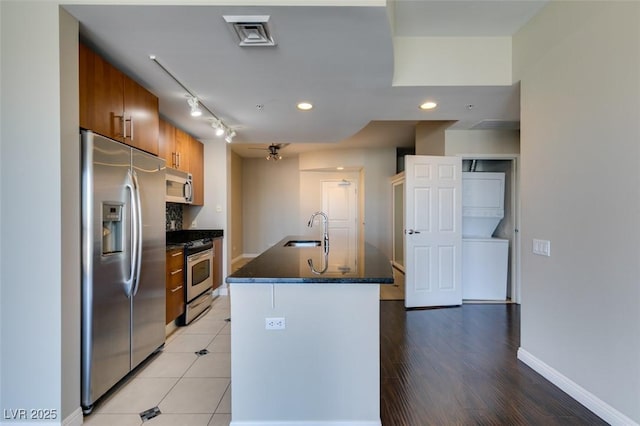 kitchen featuring ceiling fan, sink, stainless steel appliances, tasteful backsplash, and an island with sink