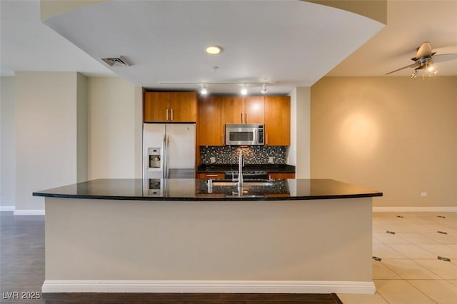 kitchen featuring decorative backsplash, ceiling fan, dark stone countertops, an island with sink, and stainless steel appliances