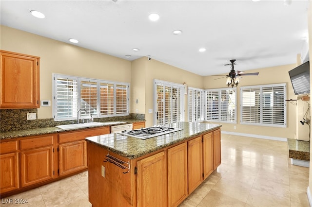 kitchen with ceiling fan, sink, a center island, dark stone countertops, and white appliances