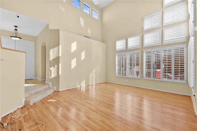 unfurnished living room with light wood-type flooring and a towering ceiling