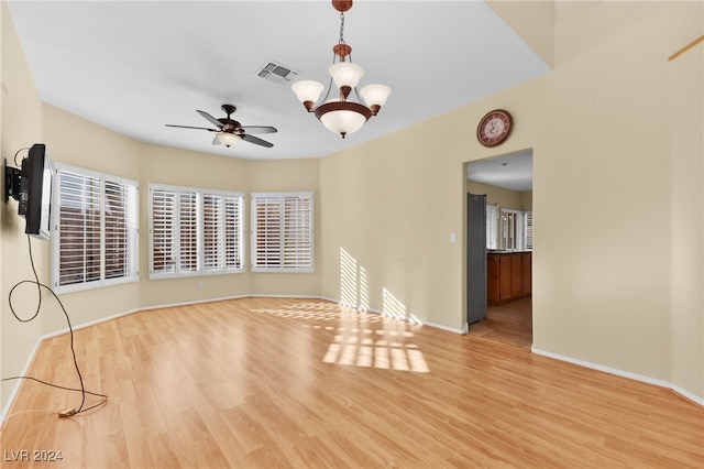 spare room with ceiling fan with notable chandelier and light wood-type flooring