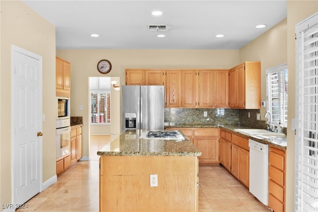 kitchen with light stone counters, light brown cabinets, a kitchen island, and appliances with stainless steel finishes