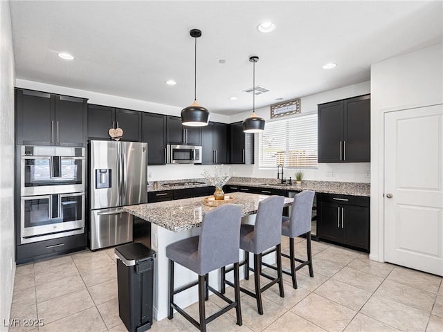 kitchen featuring a center island, hanging light fixtures, light stone counters, a breakfast bar area, and appliances with stainless steel finishes