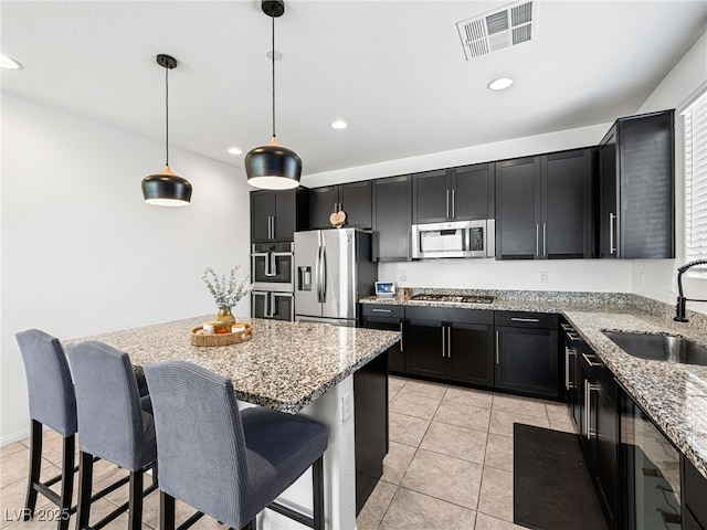 kitchen with light stone countertops, sink, stainless steel appliances, pendant lighting, and a kitchen bar