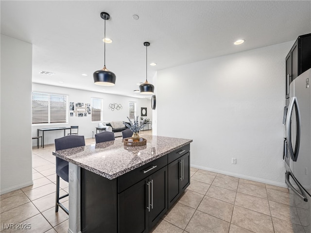 kitchen featuring stainless steel refrigerator, a center island, hanging light fixtures, a breakfast bar, and light tile patterned floors