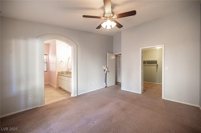 unfurnished bedroom with ensuite bath, ceiling fan, a walk in closet, light carpet, and a closet