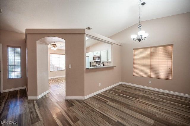 unfurnished dining area with ceiling fan with notable chandelier, vaulted ceiling, and dark wood-type flooring