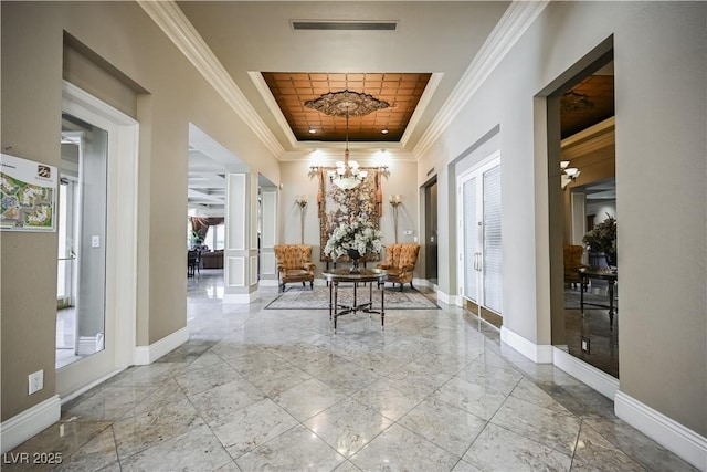 corridor featuring an inviting chandelier, baseboards, a raised ceiling, and crown molding