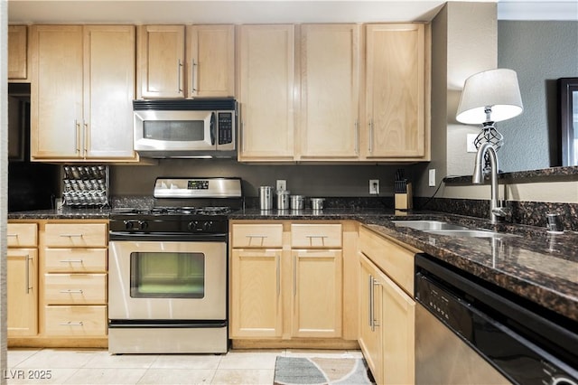 kitchen with light tile patterned floors, stainless steel appliances, light brown cabinetry, a sink, and dark stone countertops