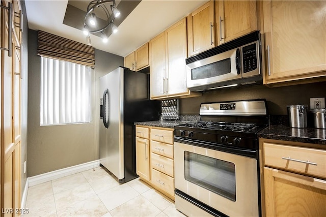 kitchen with light tile patterned floors, baseboards, dark stone counters, appliances with stainless steel finishes, and light brown cabinetry