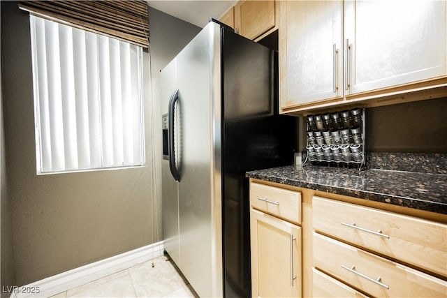 kitchen with light tile patterned flooring, baseboards, stainless steel refrigerator with ice dispenser, dark stone counters, and light brown cabinetry